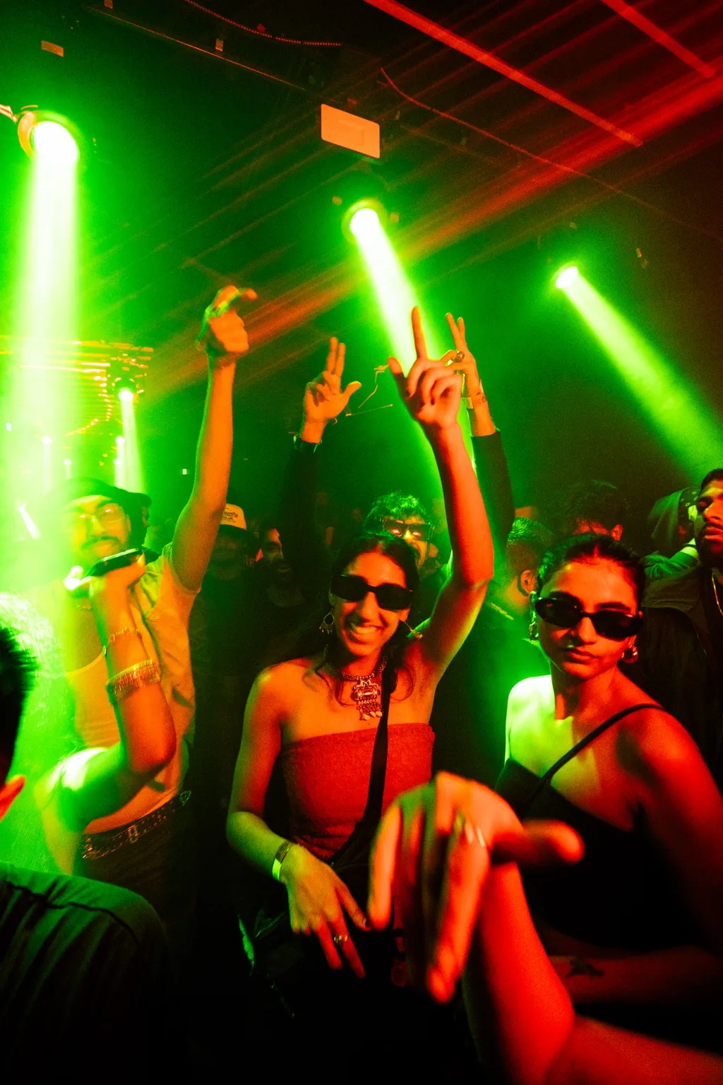 Guests dancing with raised hands under green lights at Project Kulture.