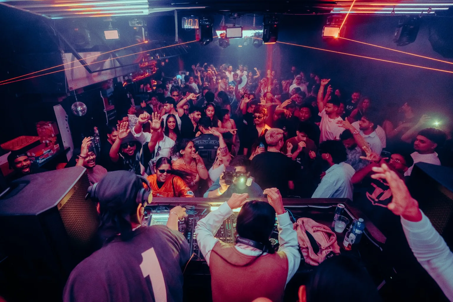 Wide view of the DJ booth and crowd beneath blue light bars at Project Kulture.